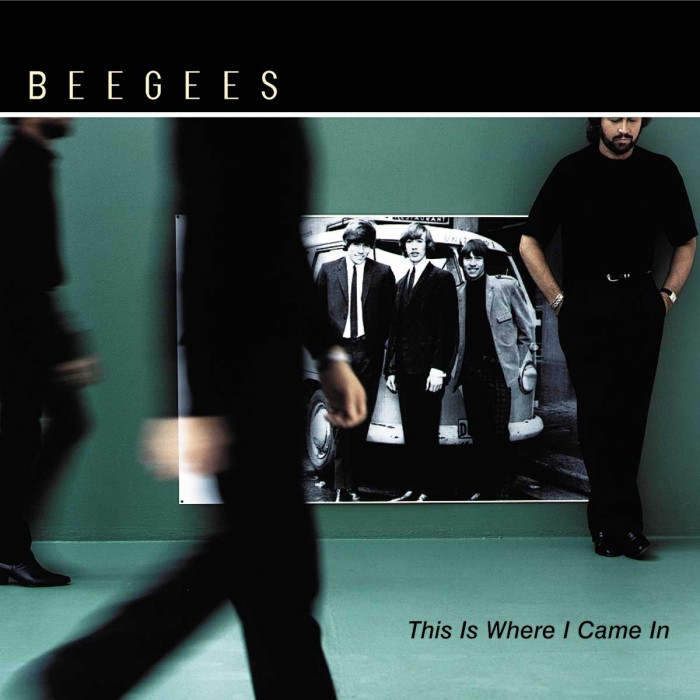 Bee Gees, this is where i came in, green floor an wall with a black and white, old photo of the brother gibb in the background, with the brothers standing in front of it, maurice and robin in blurred motion while walking and barry standing with hands in his pockets
